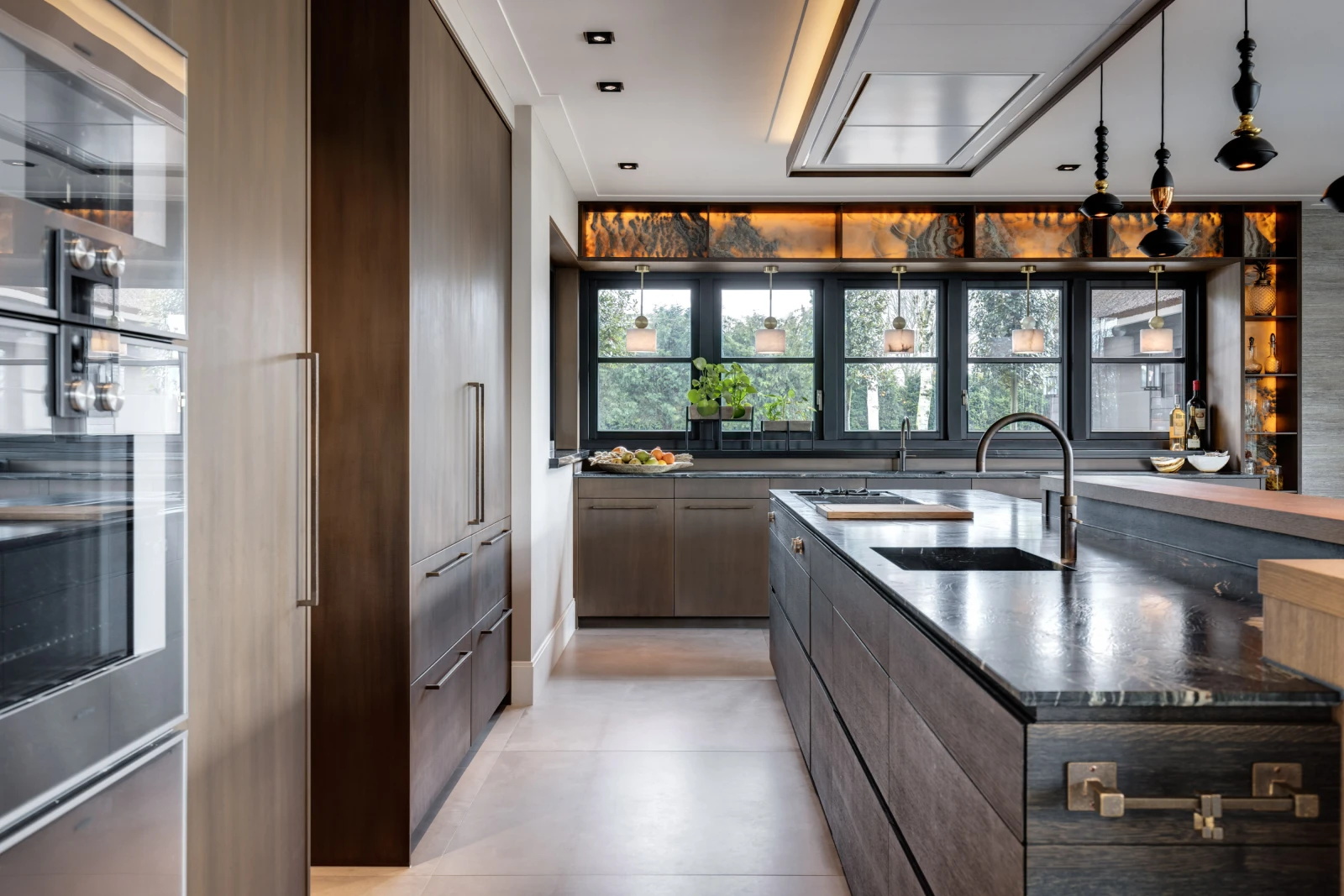 Moderne keuken met donkerhouten kasten, een groot eiland met ingebouwde spoelbak, strakke apparatuur en hanglampen. Grote ramen vullen deze exclusieve keuken met natuurlijk licht, terwijl decoratieve rekken en planten warmte toevoegen aan de ruimte.