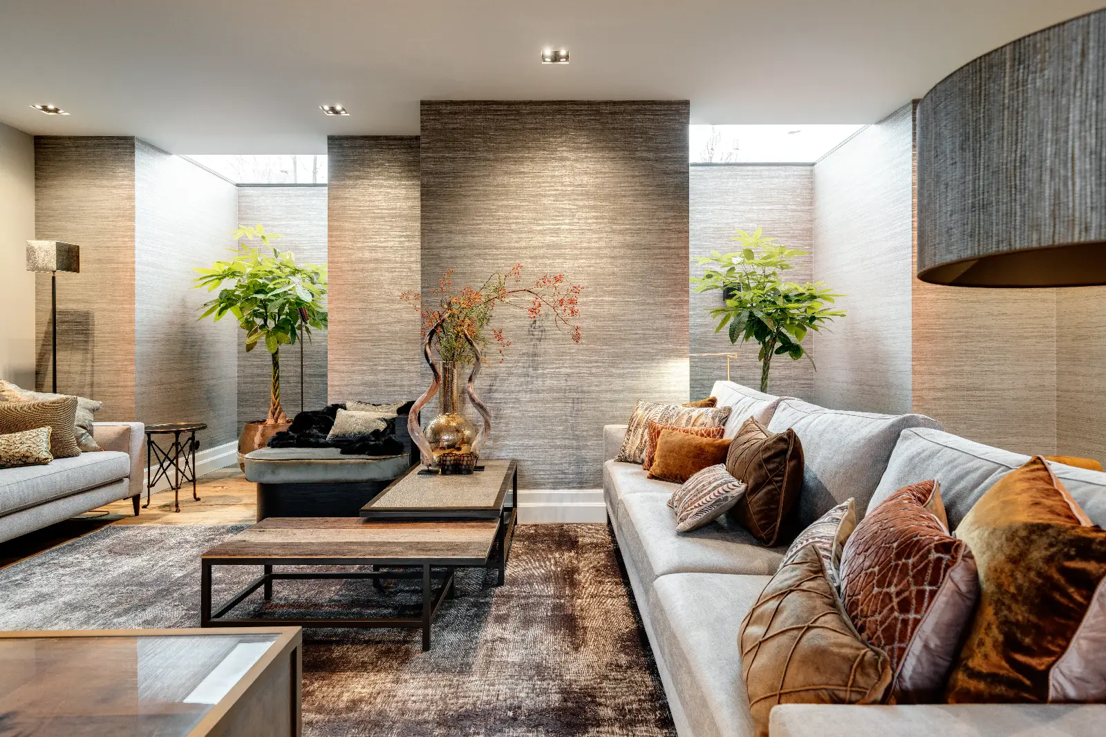 Moderne woonkamer met neutrale tinten, gestructureerde muren, grote banken met kussens met verschillende patronen, een salontafel, decoratieve vazen en hoge groene planten bij de ramen - een uitnodigende interieur woonboerderij geïnspireerd door natuurlijk licht.