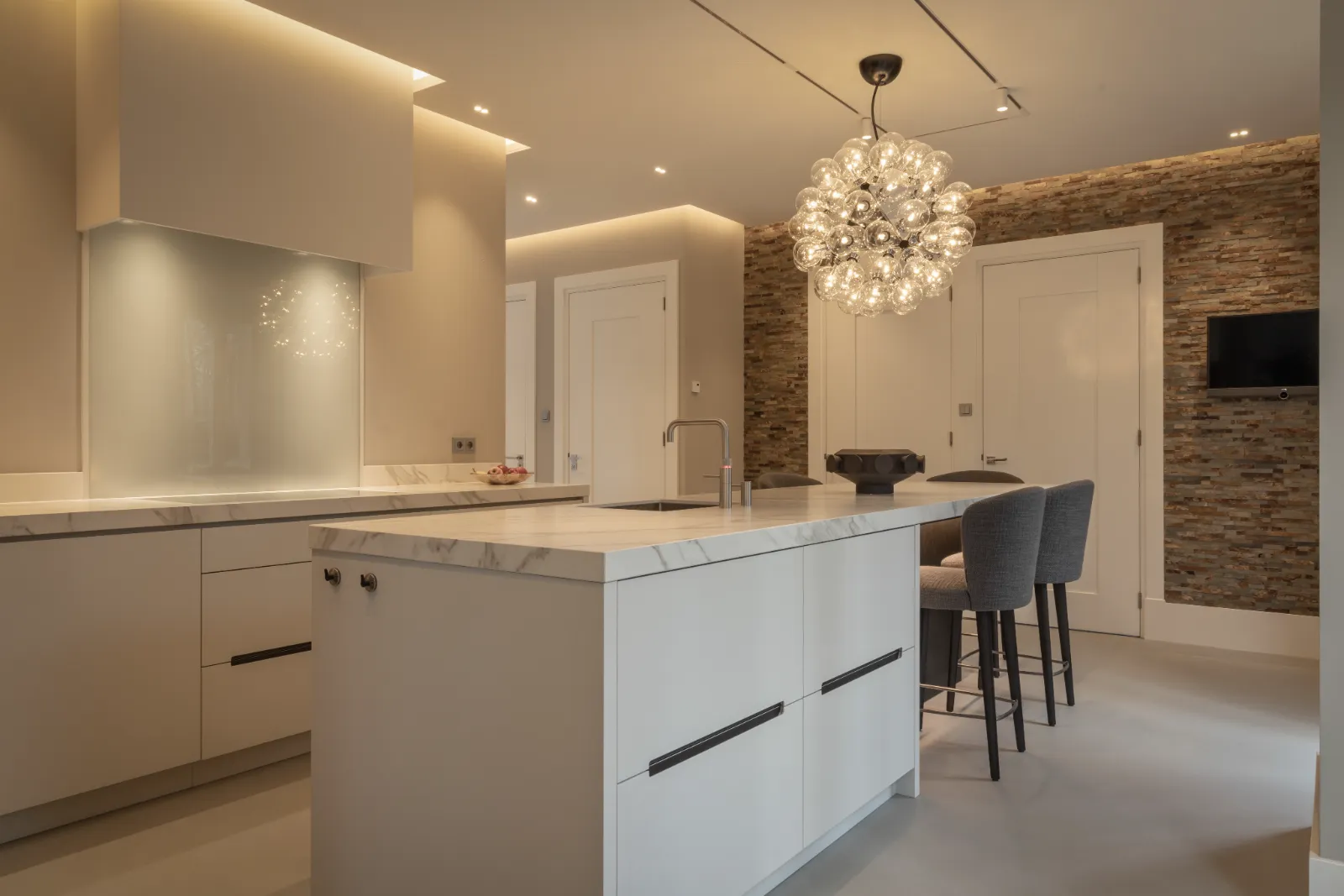 Witte luxe design keuken met marmeren werkbladen, strakke greeploze kasten, moderne inbouwapparatuur en sfeervolle verlichting.