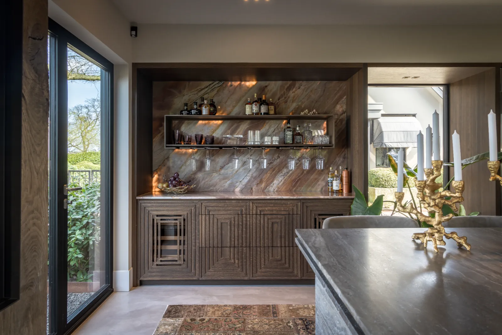 Luxe design keukens in een warme bruine houttint met marmeren achterwand, gouden kandelaars en luxe afwerking.