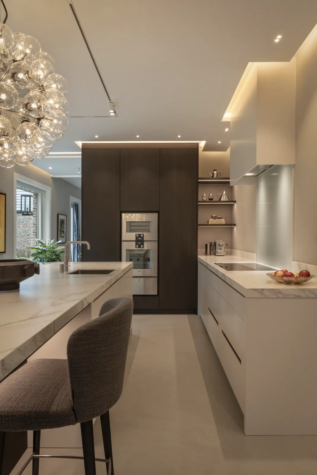 Witte luxe design keuken met marmeren werkbladen, strakke greeploze kasten, moderne inbouwapparatuur en sfeervolle verlichting.