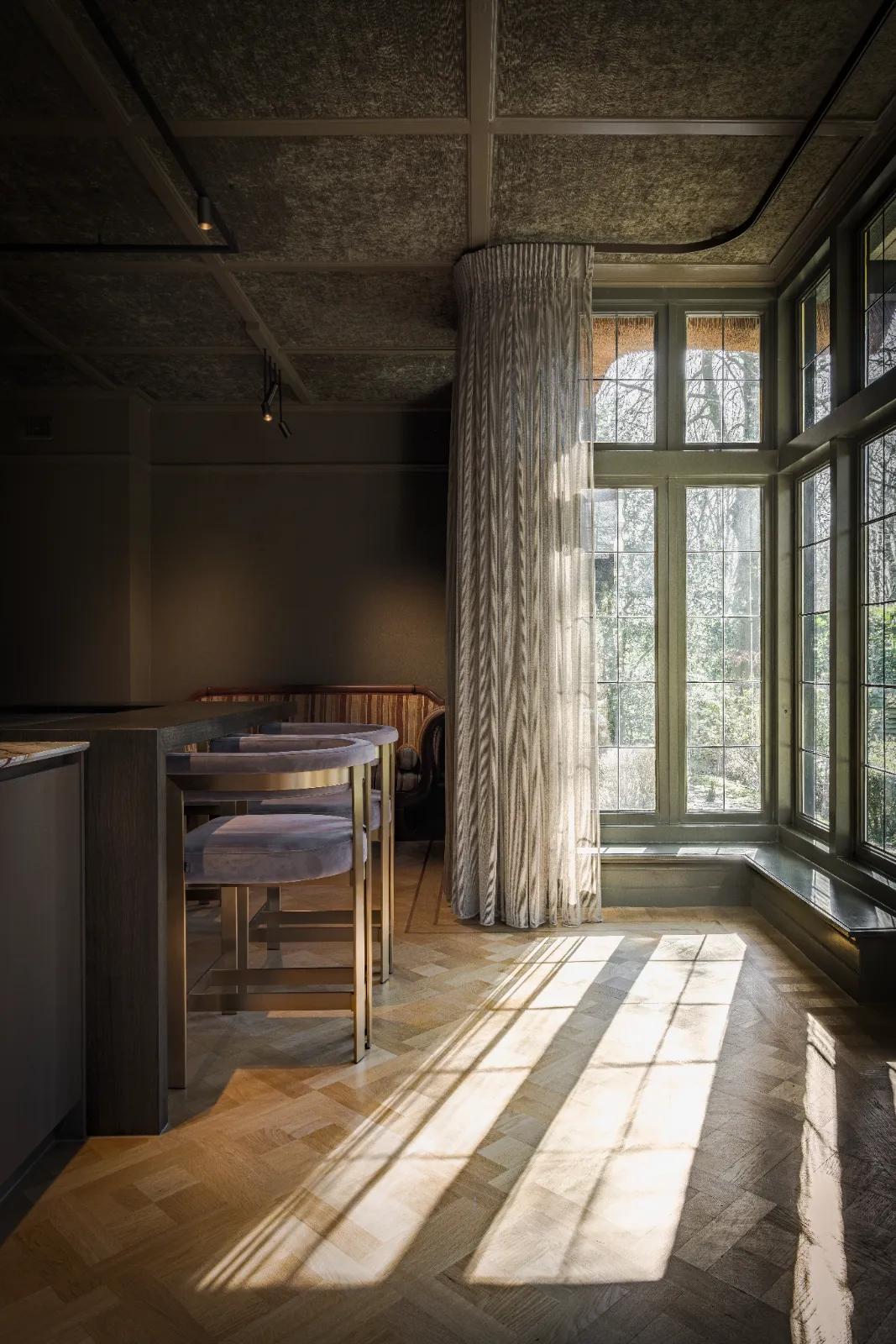 Elegante design keuken met groot raam en stijlvolle gordijnen, een kookeiland met barkrukken en een warme, uitnodigende ambiance.