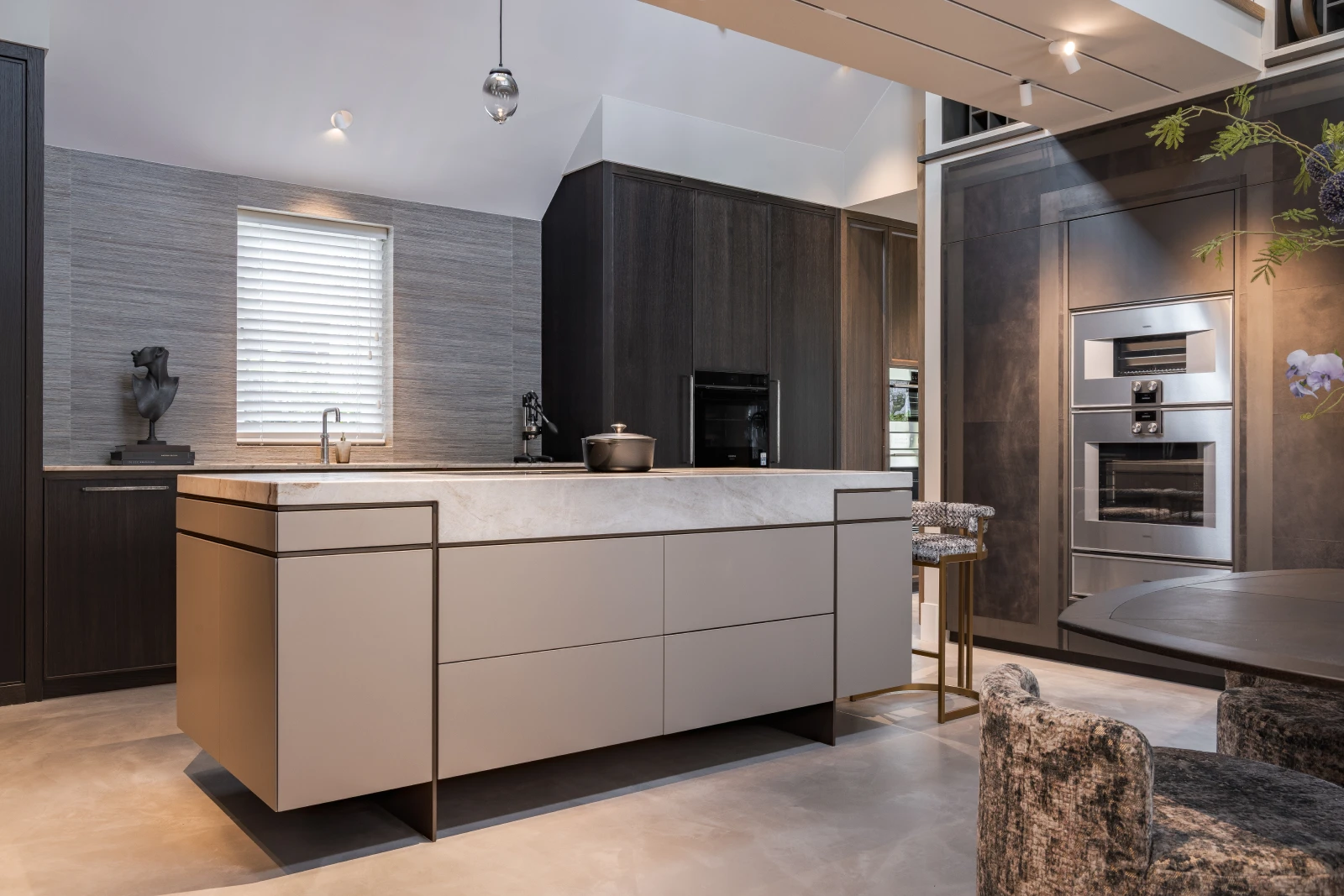 Moderne keuken in een woonboerderij met een groot centraal eiland, strakke donkere kasten, ingebouwde apparatuur, minimalistische decoratie, klein raam met jaloezieën en zachte plafondverlichting.