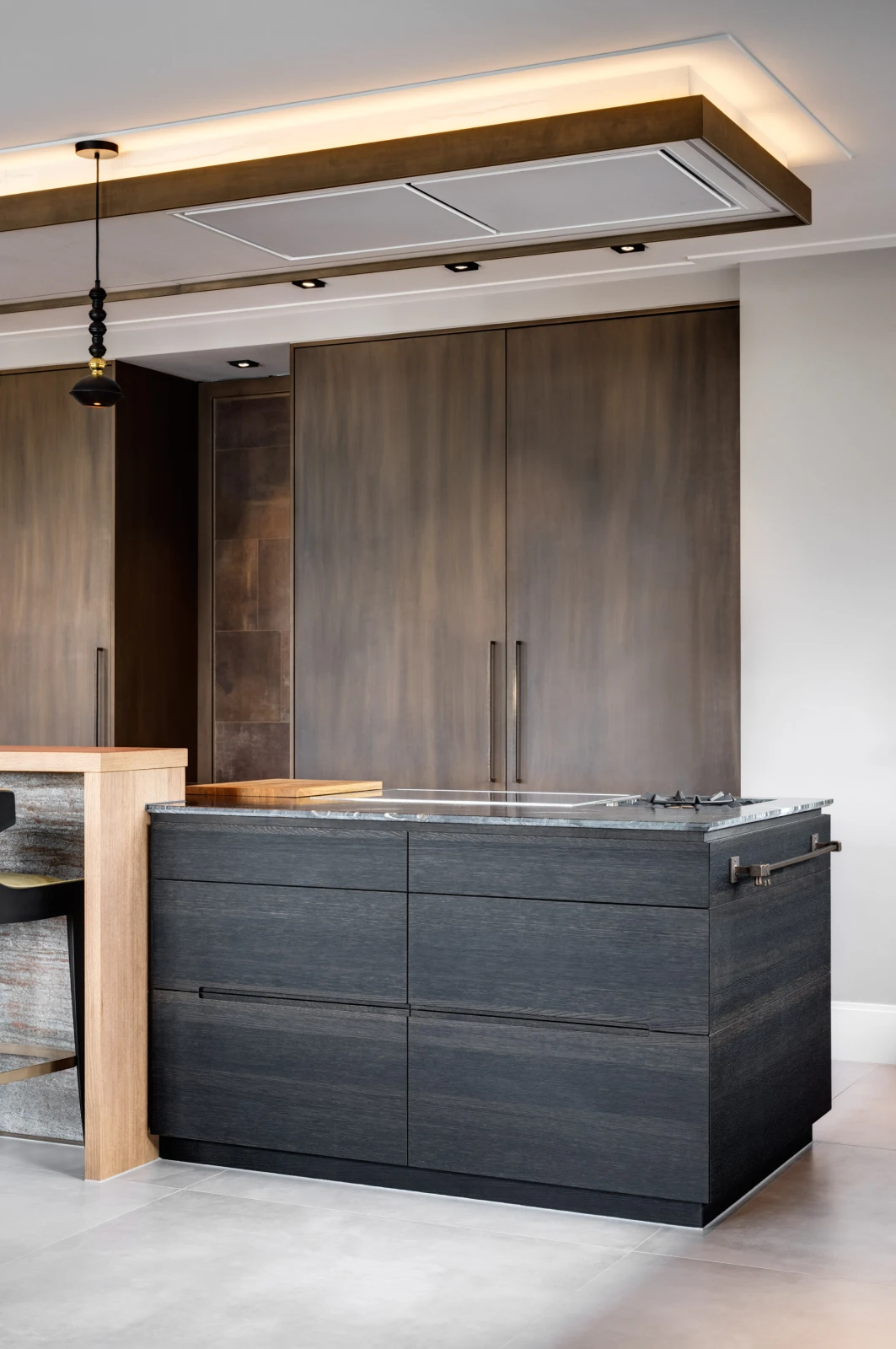 Moderne maatwerk keuken met donkerhouten kasten, een bijpassend eiland met een marmeren aanrechtblad, ingebouwde kookplaat en minimalistische hangverlichting. Neutrale tinten zorgen voor een strakke en eigentijdse look.