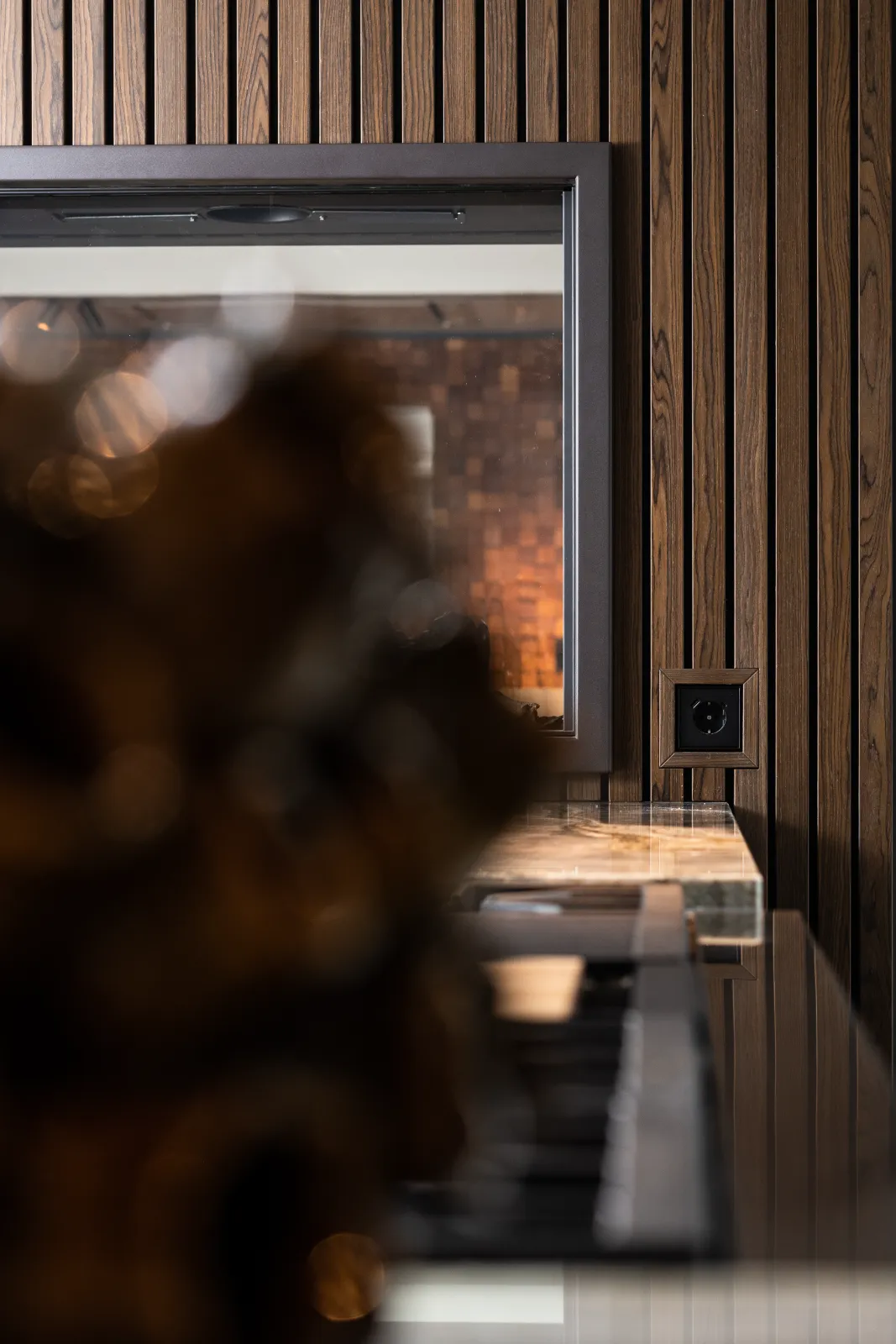 Een close-up van een modern interieur van architect keuken, met verticale houten wandpanelen, een grote ingelijste spiegel, een stopcontact en een vaag decoratief object op de voorgrond.