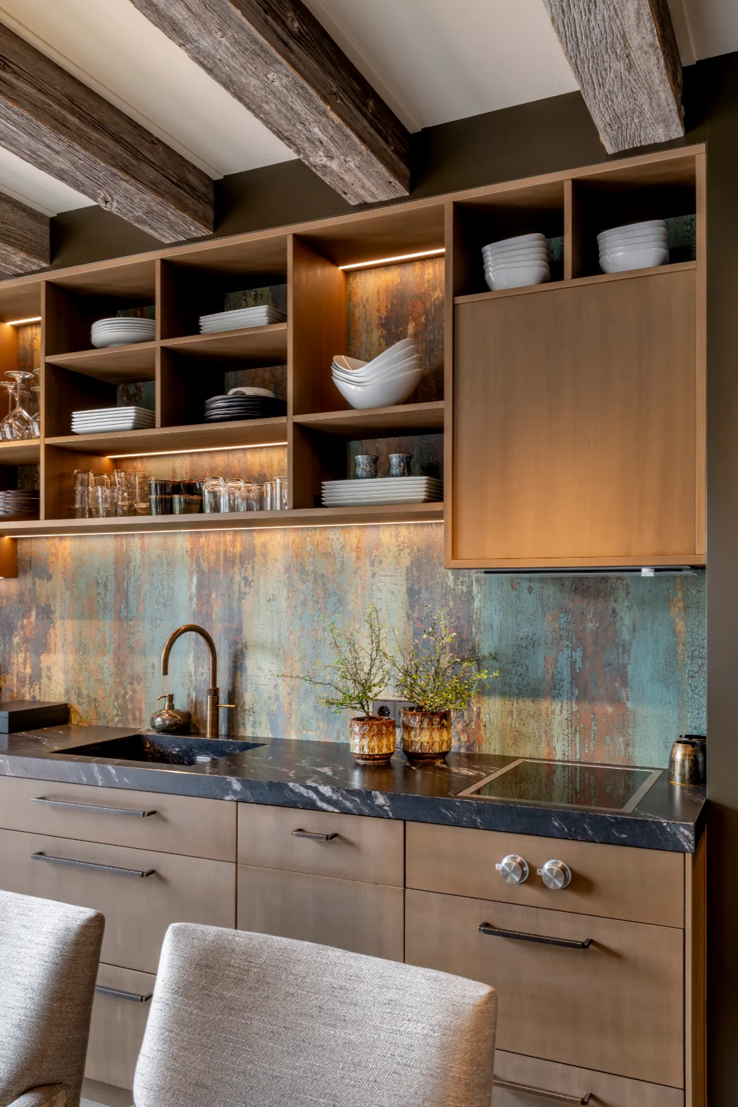 Moderne keuken in een stijlvol interieur woonboerderij, met open houten planken vol servies, zwart marmeren aanrecht, ingebouwde kookplaat, rustieke balken en een kleurrijke vintage metalen backsplash.